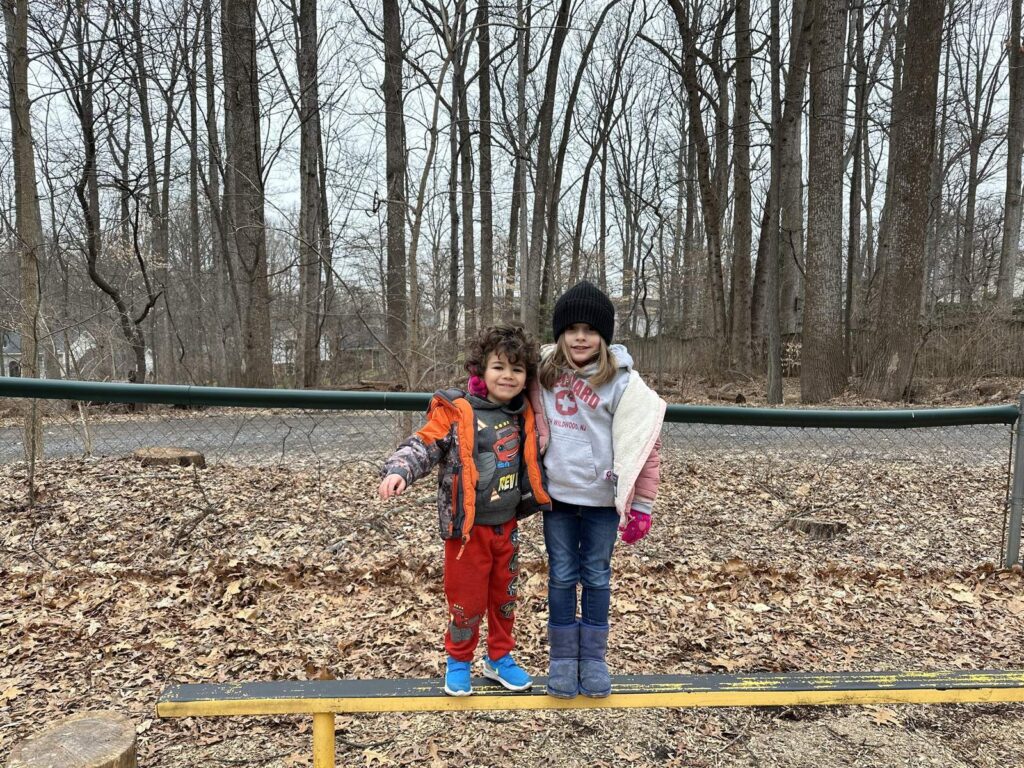Two preschoolers balancing on a beam in the wooded playground